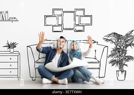 Mann aus dem Nahen Osten und muslimische Frau im Hijab, die Grundrisse halten und die Hände heben und sich vorstellen, während sie auf dem Boden sitzen, vor einem Schwarzweißbild o.... Stockfoto