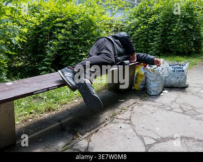 Obdachloser, der in einem Park auf einer Holzbank schläft, mit seinen Sachen in Plastiktüten während eines Tages in der Tschechischen Republik Stockfoto
