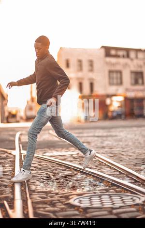 Afrikanisch-afrikanischer junger Mann, der über Eisenbahnschienen springt Stockfoto