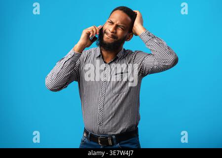 Enttäuschter Schwarzer, der einen Anruf hatte, der sich seinen Kopf schnappte, während er im Studio vor blauem Hintergrund stand Stockfoto