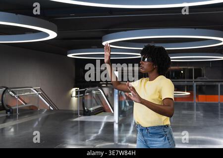 Schwarze Frau mit Afro, die eine futuristische, intelligente Brille trägt, während sie in einem Gebäude steht Stockfoto