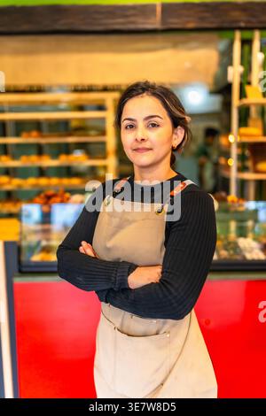 Hispanischer Bäcker mit Schürze, stehend mit gekreuzten Armen in der Bäckerei Stockfoto