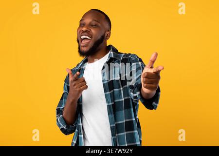 Fröhlicher Schwarzer, der die Finger wegzeigt, während er im Studio vor gelbem Hintergrund steht Stockfoto