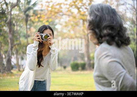 Asiatische Frau fotografiert ihre Großmutter tagsüber auf dem Rasen im Park Stockfoto