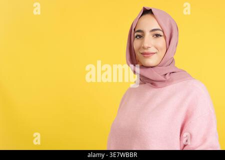 Lächelnde muslimische Frau im Hijab, die vor gelbem Hintergrund steht Stockfoto
