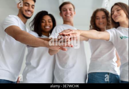 Eine lächelnde Gruppe Freiwilliger stapelt sich die Hände zusammen, während sie im Studio gegen die weiße Wand stehen Stockfoto