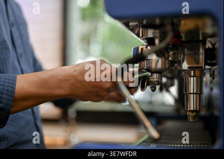 Asiatischer männlicher Barista, der im Café einen Portafilter verwendet, um Espresso auf einer Espressomaschine zu schießen Stockfoto