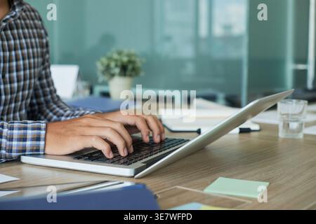 Zugeschnittenes Bild eines männlichen asiatischen Designers, der am Laptop arbeitet, während er am Schreibtisch im Büro sitzt Stockfoto