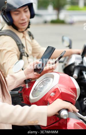 Asiatische Freunde mit Smartphones, die tagsüber auf Motorrädern auf der Stadtstraße sitzen Stockfoto