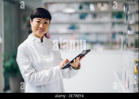 Japanische Apothekerin mit Tablette, die in der Apotheke gegen den Tresen steht Stockfoto