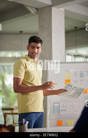 Indischer männlicher Designer steht und bespricht die neue mobile App-Schnittstelle während des Meetings im Büro Stockfoto
