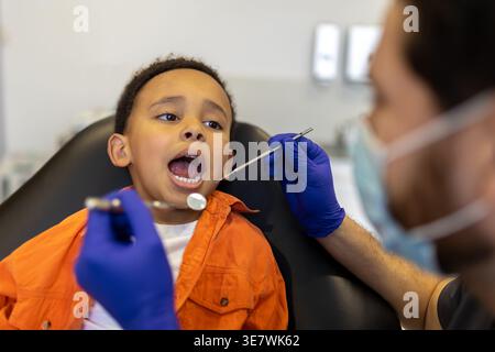 Schwarzer Junge bei zahnärztlicher Behandlung mit kaukasischem Zahnarzt in der Klinik Stockfoto
