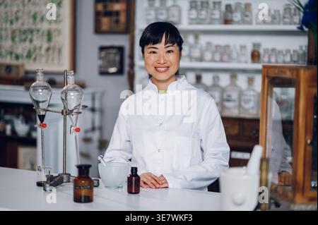Japanische Apothekerin, die mit Händen auf der Arbeitsheke steht, mit Mörtel, Stößel, Trenntrichtern und Chemikalienflaschen im Jahrgang ... Stockfoto