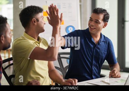 Fröhliche asiatische männliche Designer geben während des Tages im Büro High-Five Stockfoto