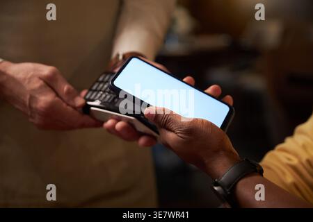 Schwarzer Mann, der mit dem Smartphone an einen kaukasischen Kellner bezahlt, der im Café steht Stockfoto