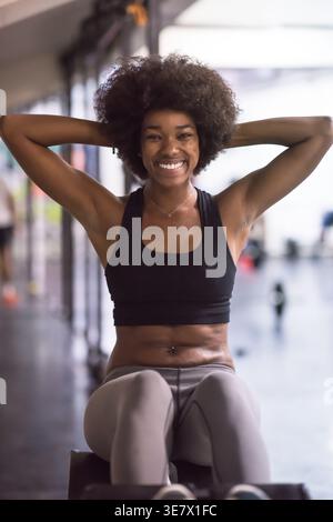Fröhliche schwarze Frau mit Afro-Kleidung, die auf der bauchbank im Fitnessstudio Sit-ups-Übungen macht Stockfoto