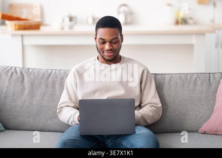 Schwarzer männlicher Freelancer, der zu Hause im Wohnzimmer auf der Couch sitzt Stockfoto
