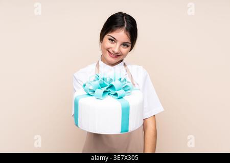 Hispanische Konditorin zeigt Kuchen, der vor beigefarbenem Hintergrund im Studio steht Stockfoto