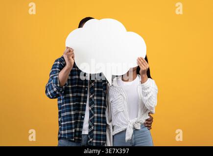 Schwarzes Paar, das hinter Luftpolsterpappe vor gelbem Hintergrund im Studio steht Stockfoto