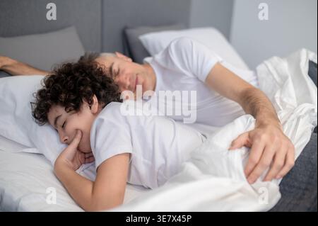 Arabischer Junge, der friedlich mit seinem Vater zu Hause im Bett schläft Stockfoto