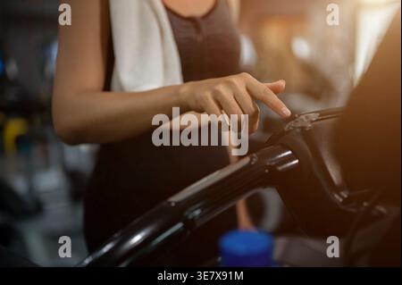 Thailändische Frau in Fitnesskleidung passt ihr Laufprogramm auf dem Laufband im Fitnessstudio an Stockfoto