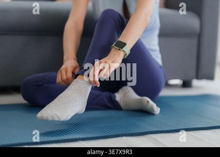 Asiatische Erwachsene Frau sitzt auf einer Yogamatte und bereitet sich auf das Training vor. Sie passt ihre sportliche Socke an, um die Bereitschaft zum Training zu demonstrieren Stockfoto