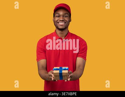 Schwarzer Mann mit Mütze, der Geschenk hält, steht vor gelbem Hintergrund im Studio Stockfoto