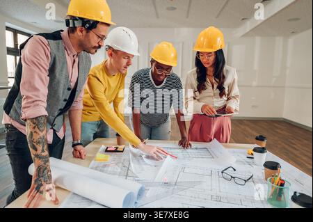 Nahaufnahme einer Gruppe von Architekten mit Schutzhelmen, die mit Blaupausen auf dem Tisch im Büro arbeiten Stockfoto