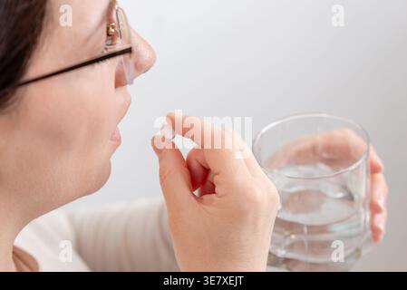 Nahaufnahme einer Frau, die eine Pille in Mundnähe mit einem Glas Wasser hält, Medikamenteneinnahmekonzept Stockfoto