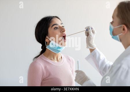Kranke indische Frau mit Gesichtsmaske, die vom Arzt abgewischt wird, während sie auf dem Stuhl in der Klinik sitzt Stockfoto