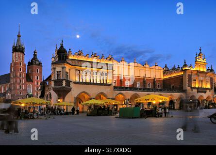 Die Leute laufen auf dem Marktplatz von Krakau, während die Sonne untergeht. Die alten Gebäude leuchten am Abendhimmel auf. Stockfoto