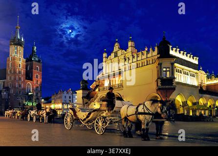 Die Menschen genießen den Abend in Krakau, während eine Pferdekutsche in der Nähe des Marktplatzes wartet. Der Mond scheint über den historischen Gebäuden. Stockfoto