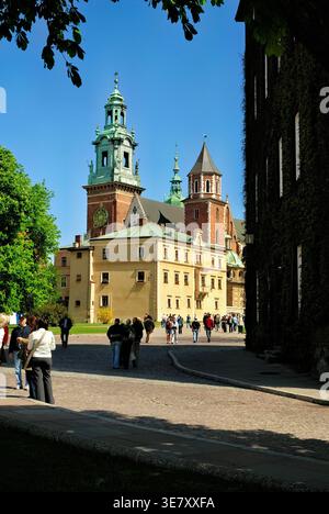 Besucher schlendern auf einem Pfad in der Nähe der Burg Wawel in Krakau, Polen, und genießen den klaren Himmel und das warme Wetter während des Tages. Stockfoto