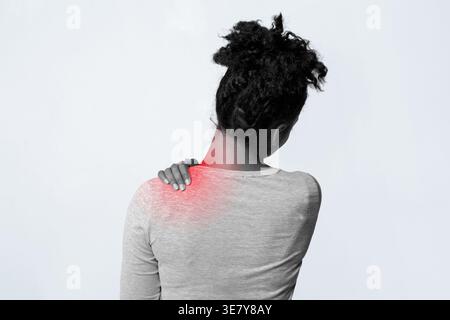 Schwarze Frau, die an Schulterschmerzen leidet, während sie vor weißem Hintergrund im Studio steht Stockfoto