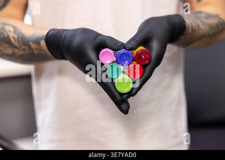 Asiatischer männlicher Tätowierer mit Latexhandschuhen mit verschiedenfarbigen Tinten, die sich auf die Tätowierung im Studio vorbereiten Stockfoto