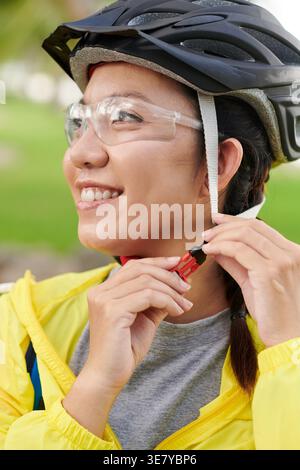 Lächelnde asiatische Radfahrerin mit Fahrradhelm im Park Stockfoto