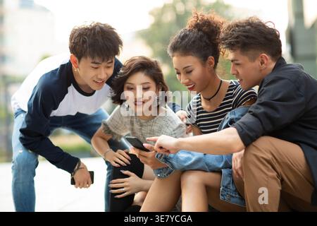 Lächelnde Gruppe chinesischer Freunde, die tagsüber auf der Straße sitzen Stockfoto