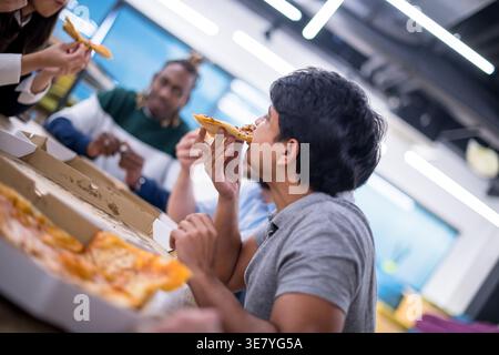 Verschiedene Geschäftsleute essen gemeinsam Pizza, während sie am Tisch sitzen und die Mittagspause im Büro genießen Stockfoto