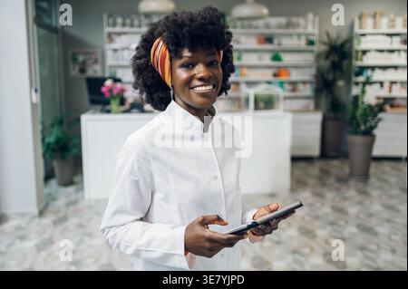 Schwarzer weiblicher Apotheker mit Afro-Tablette, die in der Apotheke gegen den Zähler steht Stockfoto