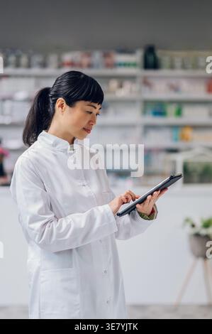 Japanische Apothekerin mit Tablette, die in der Apotheke gegen den Zähler steht Stockfoto
