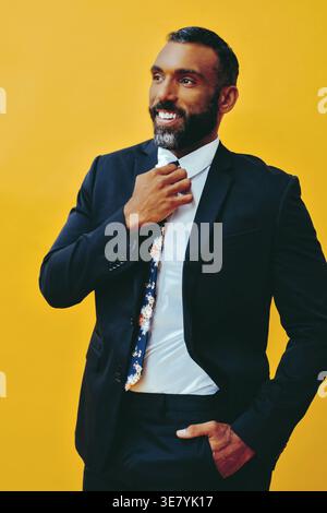 Bärtiger Geschäftsmann im Anzug, der seine Krawatte fixiert und wegblickt mit Hand in der Tasche vor gelbem Hintergrund im Studio Stockfoto