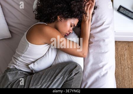 Deprimierte hispanische Frau weint, während sie das Kissen umarmt, das zu Hause auf dem Bett liegt Stockfoto