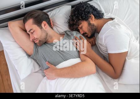 Indische und kaukasische Schwule schlafen zusammen im Bett zu Hause Stockfoto