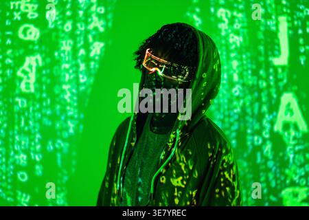 Serious Black man trägt einen Hoodie und führte Augmented Reality Brillen, die wegschauen, während sie in einem dunklen Raum mit grünen Neonlichtern stehen Stockfoto