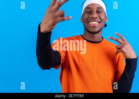 Lächelnder schwarzer Mann in orangefarbenem Hemd mit Rock-and-Roll-Schild, das auf blauem Hintergrund steht Stockfoto