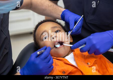 Schwarzer Junge bei Zahnbehandlung mit männlichen Zahnärzten in der Klinik Stockfoto