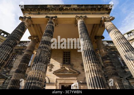 Ein flacher Blick auf einen großen neoklassizistischen Gebäudeeingang mit großen kannelierten Säulen und komplizierten Mauerwerken, mit einem hellblauen Himmel über dem Dach Stockfoto