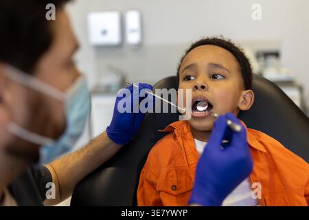 Schwarzer Junge bei zahnärztlicher Behandlung mit kaukasischem Zahnarzt in der Klinik Stockfoto