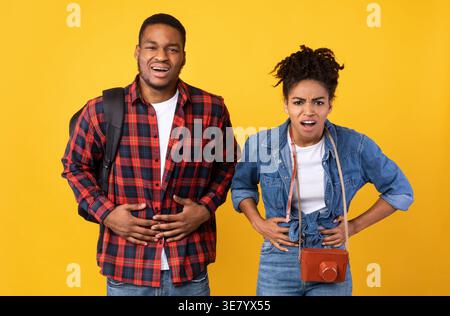 Schwarzes Reisepaar Mit Bauchschmerzen Nach Lebensmittelvergiftung Auf Urlaub Stehend Über Gelbem Studio Hintergrund. Tr.... Stockfoto