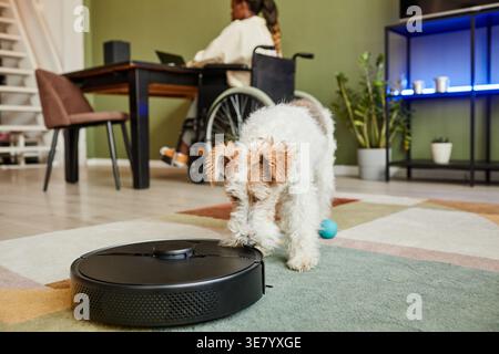 Behinderte Schwarze Frau im Rollstuhl, die an einem Laptop arbeitet, am Tisch neben dem Hund zu Hause sitzt Stockfoto